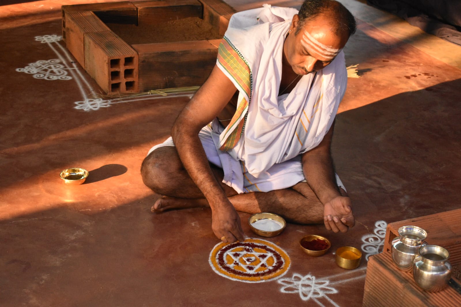 Vedic Purohit handcrafting sacred mandala rangoli beside homa kunda
